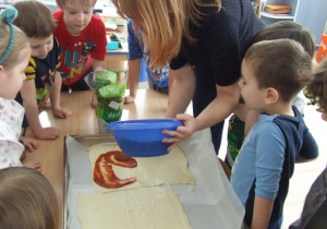 Nauczycielka rozsmarowuje sos na cieście do pizzy.