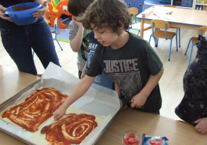 Dzieci rozsmarowują sos na cieście do pizzy.
