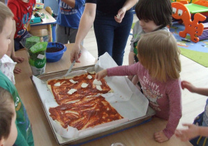 Dziewczynka kładzie plastry mozzarelli na ciasto.