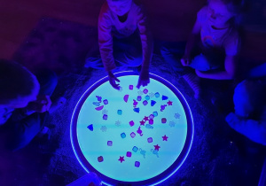 Dzieci bawią się na świetlistej planszy plastykowymi zwierzątkami.