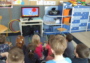 Dzieci siedzą i oglądają bajkę muzyczną.