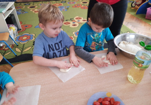 Dzieci na papierach do pieczenia formują swoją małą pizzę.