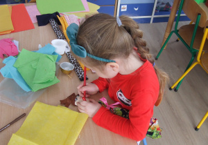 Dziewczynka rysuje mazakiem usta na łyżce drewnianej.