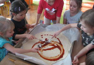 Dzieci smarują sosem spód do pizzy.