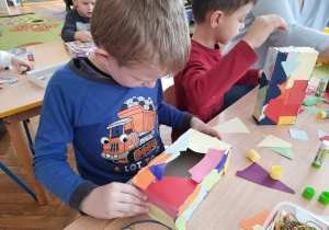Chłopcy wyklejają pudełko papierem kolorowym.