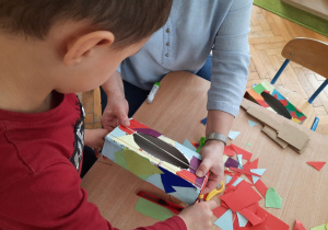 Chłopiec wykleja pudełko papierem kolorowym.