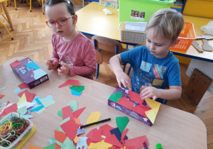 Dzieci wyklejają pudełka papierem kolorowym.