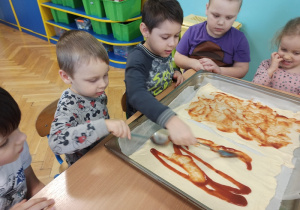 Dzieci smarują sosem pizzę
