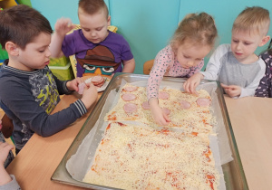 Dzieci posypują pizzę serem