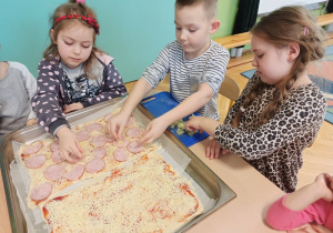 Dzieci układają szynke na pizzy