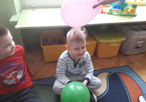 Chłopiec siedzi na dywanie trzymając balon w ręku. Ma naelektryzowane włosy.