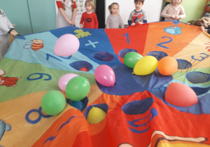 Dzieci trzymają chustę animacyjną i odbijają balony.