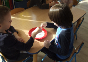 Dzieci maczają patyczki w mleku i kolorowym tuszu.