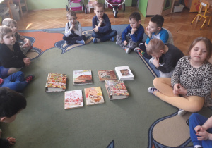 Dzieci siedzą na dywanie, przed nimi leżą książki kucharskie.