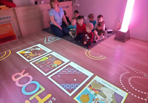 Nauczycielka opowiada dzieciom reguły korzystania z podłogi interaktywnej.