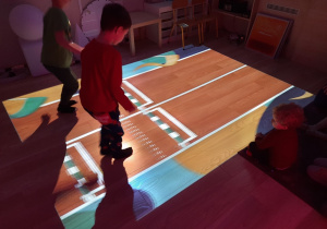 Chłopcy na podłodze interaktywnej bawią się na bieżni biegowej.