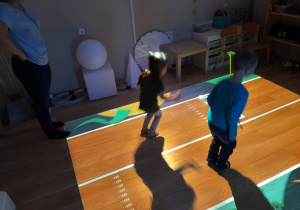Dzieci na podłodze interaktywnej bawią się na bieżni biegowej.