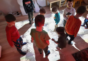 Dzieci na podłodze interaktywnej bawią się w sprzatanie śnieżynek.