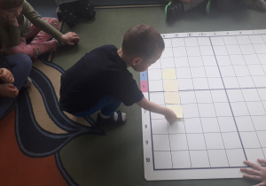 Chłopiec kładzie żółtą karteczkę na odpowiednim polu planszy.
