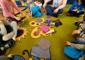 Dzieci układają mozaikę z materiałów na dywanie.