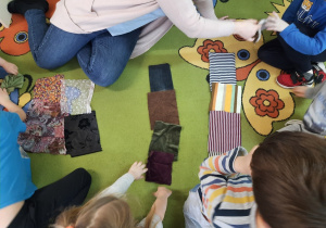 Dzieci układają mozaikę z materiałów na dywanie.