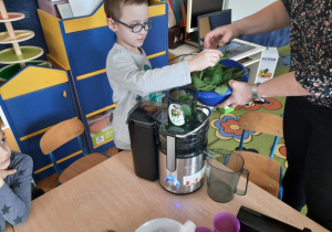Chłopiec wkłada szpinak do sokowirówki.