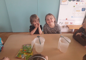 Dziewczynki siedzą przy stole, na którym znajdują się produkty potrzebne do przygotowania galaretki.