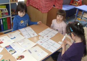 Dzieci przy stoliku dobierają odpowiednie ilustracje - karta pracy.