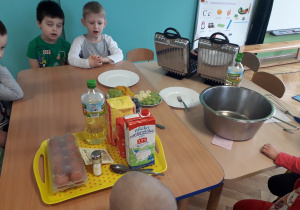 Dzieci siedzą przy stole, na którym znajdują się produkty potrzebne do zrobienia gofrów.