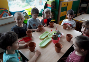 Dzieci siedzą przy stole, a na nim ustawione akcesoria do sadzenia