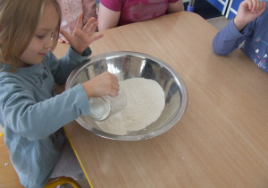 Dziewczynka wpisuje mąkę do miski.