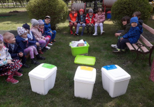 Dzieci siedzą na ławkach, przed nimi pojemniki do segregacji śmieci