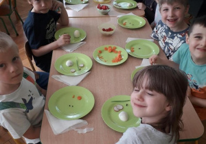 Dzieci siedzą przy stole i wykonują figurki z jajek