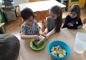 Dzieci trą jabłka na tarce.