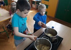 Chłopcy wlewają sok jabłkowy do garnków.