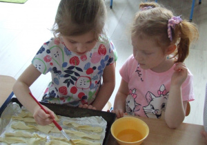 Dziewczynka maluje ciasto jajkiem.