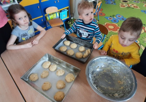Dzieci układaja bułeczki na formie do pieczenia.