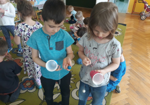 Dzieci przymocowują sznureczek do kubka.