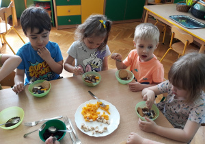 Dzieci jedzą budyń z owocami.
