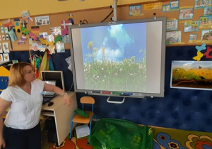 Nauczycielka pokazuje na tablicy multimedialnej kwiaty na łące majowej.