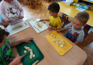 Dzieci kroją na desce banany do dekoracji budyniu.