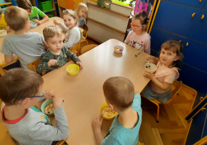 Dzieci zjadają przy stolikach budyń.
