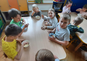 Dzieci zjadają przy stolikach budyń.