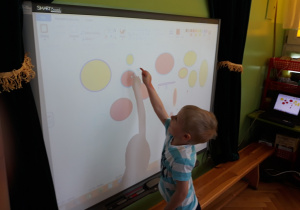 Dziecko rysuje figury na tablicy multimedialnej.