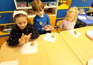 Dzieci roluja kuleczki z masy bananowo- herbatnikowej w dłoniach.
