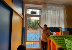 Nauczycielka pokazuje na sali piktogram wyjścia ewakuacyjnego i objaśnia jego znaczenie.