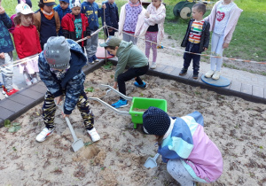 Dzieci nasypują piasek do taczki.