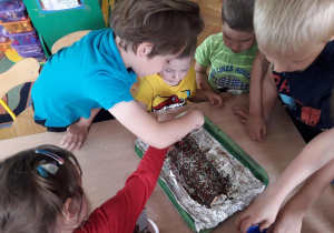 Dzieci polewają deser czekoladą i posypują posypką.