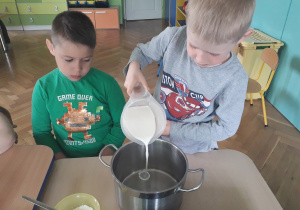 Chłopiec wlewa mleko do garnka.