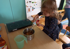 Dziewczynka wlewa sok jabłkowy do garnka.